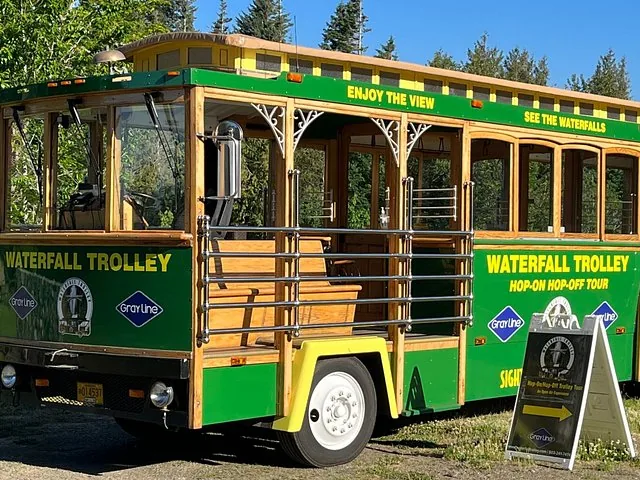 A green open-air Waterfall Trolley parked on a sunny day