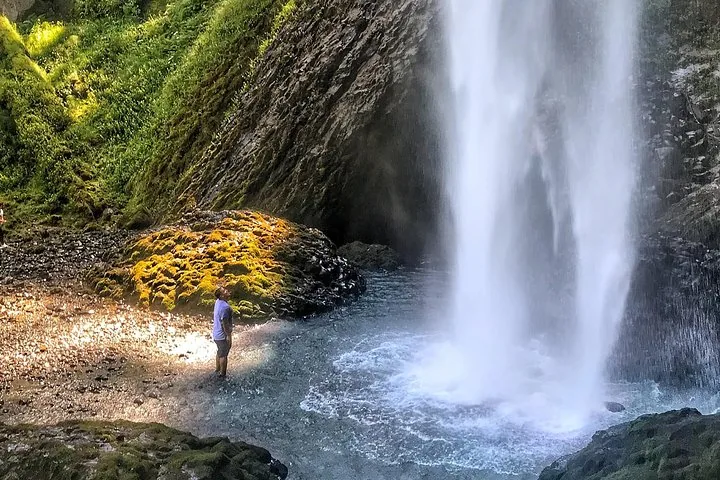 Una persona in piedi alla base di una potente cascata avvolta nella nebbia