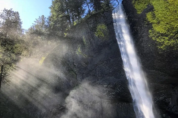 Sonnenstrahlen, die am Fuß eines Wasserfalls durch die Gischt scheinen